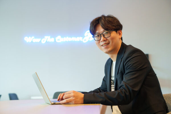 a man poses in front of a Coupang logo wall.